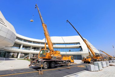 İki sarı turna modern binanın yanında malzeme kaldırıyor.