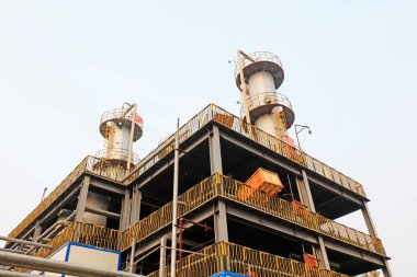 İki uzun bacası ve iskelesi olan sanayi binası.