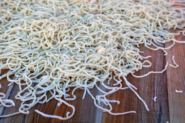 Pişmemiş erişteler yakın planda ahşap yüzeye saçılmış.