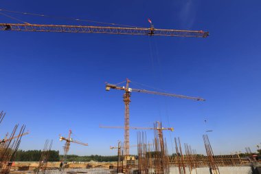 Açık mavi gökyüzüne karşı çeşitli vinçlerin yer aldığı inşaat alanı