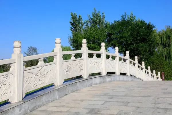 Yeşil ağaçlarla çevrili taş köprü yolu boyunca kıvrılıyor.