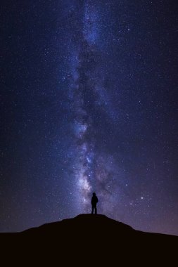 Samanyolu manzarası, yıldızlı gece gökyüzü ve yüksek dağların tepesinde duran insan silueti.
