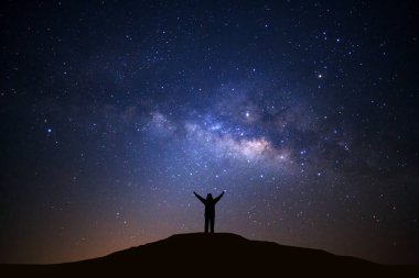 Samanyolu manzarası, yıldızlı gece gökyüzü ve yüksek dağların tepesinde duran insan silueti.