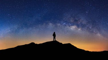 Samanyolu ile Panorama manzarası, yıldızlı gece gökyüzü ve yüksek dağda duran bir adamın silueti..