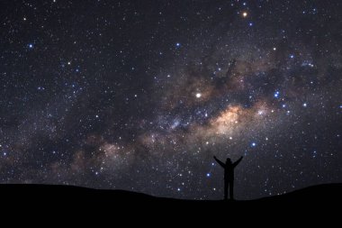 Samanyolu manzarası, yıldızlı gece gökyüzü ve yüksek dağların tepesinde duran insan silueti.