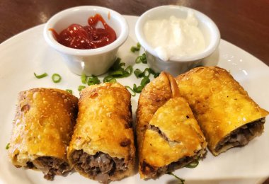 İki soslu, beyaz tabakta peynirli biftekli sandviçin yakın plan çekimi.