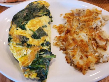 Beyaz seramik tabağın üstünde ev kızartması ve ıspanaklı omlet.