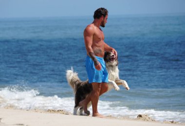 Savage Ditch, Delaware, ABD - 4 Temmuz 2023 Sahilde neşeli köpeğiyle yürüyen bir adam