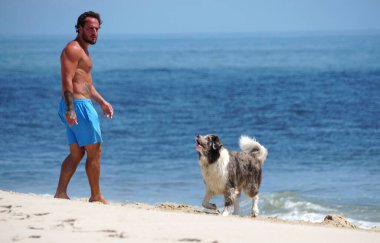 Savage Ditch, Delaware, ABD - 4 Temmuz 2023 Sahilde neşeli köpeğiyle yürüyen bir adam