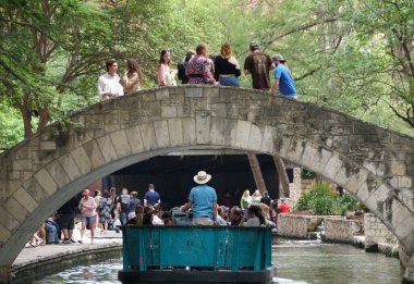 San Antonio, Teksas, ABD - 6 Nisan 2024 - Mavi renkli Rio tekne turu yolcuları nehirde taşıyor ve Selena 'nın köprüsünü geçiyor