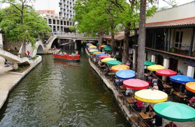 San Antonio, Teksas, ABD - 6 Nisan 2024 Restoranların renkli masa şemsiyeleri ve nehirdeki tekne