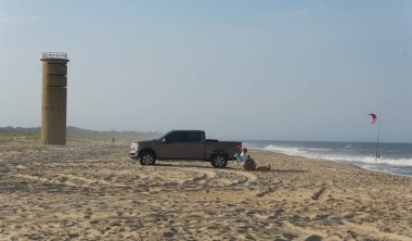 Rehoboth Beach, Delaware, ABD - 4 Temmuz 2024 - 2. Dünya Savaşı gözetleme kulesinin yanındaki sahilde bir kamyonet ve sörf balıkçısı