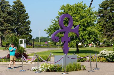 Chanhassen, Minnesota, ABD - 9 Temmuz 2024 - Paisley Park 'taki müzenin önünde şarkıcı Prince' i temsil eden mor sembolün fotoğrafını çeken bir ziyaretçi