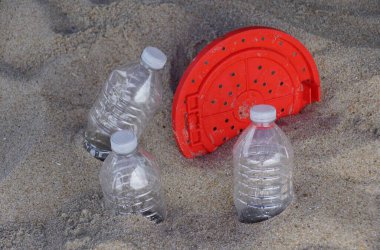 A red lid and three plastic bottles half-buried in the sand at the beach clipart