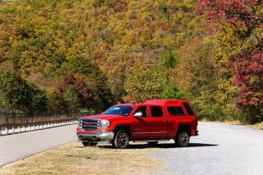 Jim Thorpe, Pennsylvania, ABD - 19 Ekim 2024 - Kırmızı GMC Sierra 4X4 kamyonu parktaki sonbahar yeşilliklerinin canlı renklerine bakıyor