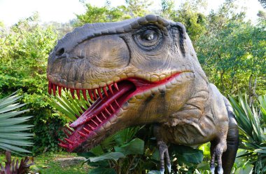 Bir T-Rex heykelinin yakın çekimi, dokulu derisi ve keskin dişleriyle karışık detaylar sergiliyor, Gunung Jerai, Kedah, Malezya yakınlarında yemyeşil ile çevrili.