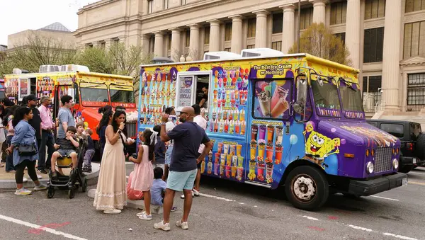 Washington D.C., ABD - 29 Mart 2025 Sıcak bir bahar gününde ziyaretçiler mobil dondurma ve meyve suyu satıcılarının etrafında toplanıyor.