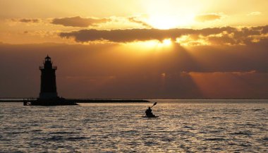 Deniz feneri ve kanoyla birlikte deniz üzerinde dramatik bir gün batımı Cape Henlopen State Park, Lewes, Delaware, ABD yakınlarında alevli gökyüzüne karşı duruyor..