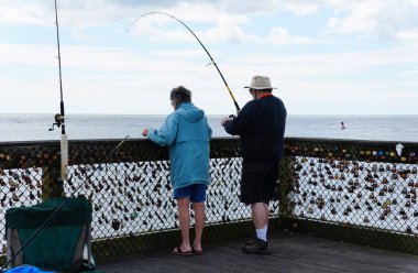 Okyanus Şehri, Maryland, ABD - 21 Mayıs 2025 Balıkçılık meraklıları okyanusa bakan bir iskelede duruyor, sayısız asma kilitle süslenmiş bir tel örgüyle.