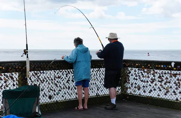 Okyanus Şehri, Maryland, ABD - 21 Mayıs 2025 Balıkçılık meraklıları okyanusa bakan bir iskelede duruyor, sayısız asma kilitle süslenmiş bir tel örgüyle.