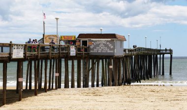 Okyanus Şehri, Maryland, ABD - 23 Mayıs 2025 - Okyanus üzerinde uzanan ahşap bir iskele, kumlu sahili ve küçük bir balıkçı kulübesini gösteriyor..