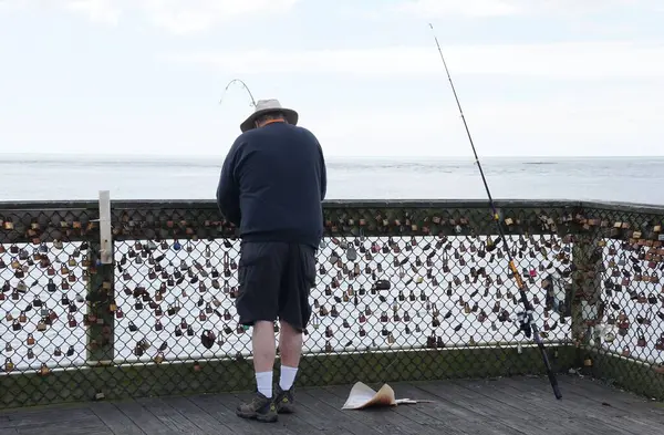 Okyanus Şehri, Maryland, ABD - 23 Mayıs 2025 - Bir balıkçı meraklısı Atlantik Okyanusu 'na bakan bir iskelede duruyor, sayısız asma kilitle süslenmiş bir tel örgüyle.