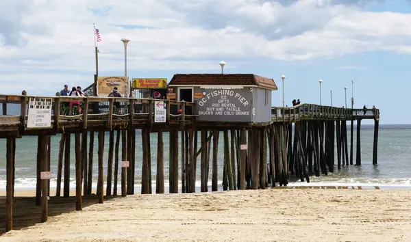 Okyanus Şehri, Maryland, ABD - 23 Mayıs 2025 - Okyanus üzerinde uzanan ahşap bir iskele, kumlu sahili ve küçük bir balıkçı kulübesini gösteriyor..