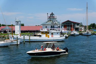 St Michaels, Maryland, ABD - 30 Haziran 2025 - Güneşli bir günde limanı ve tarihi deniz fenerini geçen küçük bir tekne