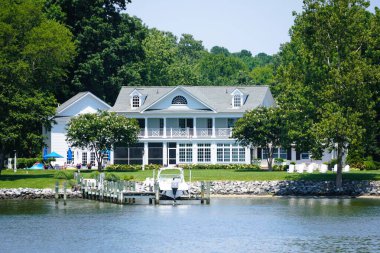 St. Michaels, Maryland, ABD - 30 Haziran 2025 Beyaz dış görünüşlü, geniş verandalı, yeşil çimenli ve limanlı lüks bir liman evi.