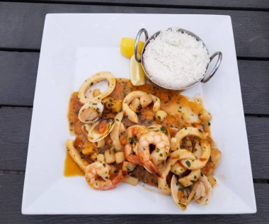 Cömert bir porsiyon sotelenmiş deniz ürünleri, karides, istiridye ve mürekkep balığı, bir kase pirincin yanında servis edilir..