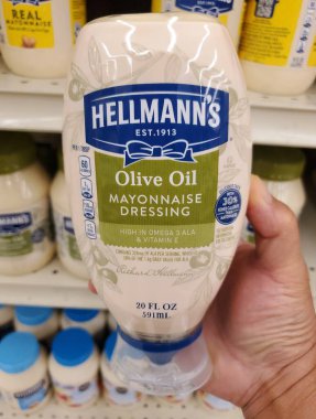 Delaware, U.S.A - Sept 30, 2025 - Hellmann's Olive Oil Mayonnaise Dressing, 20 fl oz bottle, held in a hand above shelves stocked with other mayonnaise products.