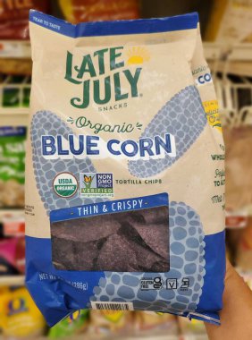 Delaware, U.S.A - Sept 30, 2025 - A bag of Late July Organic Blue Corn Thin and Crispy Tortilla Chips, held in a hand in a grocery aisle.