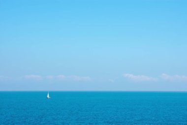 Bomboş denizde küçük bir yelkenli. Boş gökyüzü ve küçük bulutlarla.