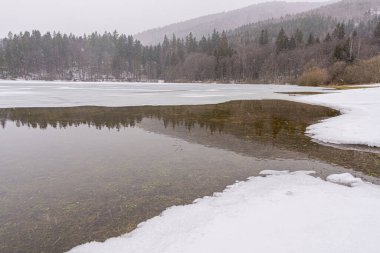 Dağlarda kısmen donmuş bir göl, karlı kış ormanlarında ağaçlarla birlikte.