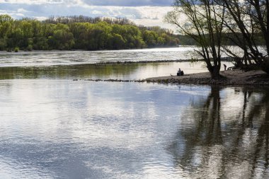 Nehir kıyısındaki uzak balıkçı, arka ışıklandırma, yansımalar, açık hava, telefoto.