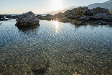 Gün batımında boş kayalık plaj, arka plan, önplanda şeffaf berrak su, Yunanistan, Girit adası, geniş açı mercek