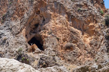Çorak kayalıklarda dev bir mağara açılıyor. Güneş ışığında dalgalanan adam, Aradena Vadisi, Yunanistan, Girit Adası, telefoto.