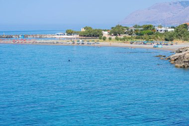 Sahilde şemsiyeler ve insanlar, arka planda evler ve dağlar, güneş, Frangokastello, Yunanistan, Girit adası, telefoto