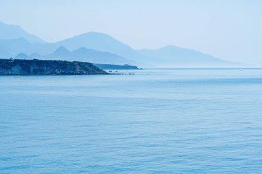 Sahil sıradağlarının silueti berrak mavi gökyüzü, Yunanistan, Girit adası ve telefoto ile durgun denizin yanında kayboluyor.