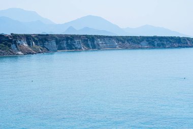 Yüksek plaj, kayalar ve sakin deniz, arka planda yüksek dağlar, güneş manzarası, Yunanistan, Girit adası, telefoto