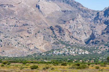 Uzakta Patsianos köyünün evleri, arka planda yüksek çorak dağlar, güneş, Yunanistan, Girit adası, telefoto lensleri.