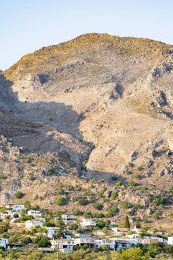 Yüksek, çorak, kayalık bir dağın eteğindeki küçük bir köyün evleri, güneşli, açık mavi gökyüzü, telefoto