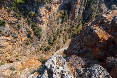 Yukarıdan dar, dik, kayalık vadi, altında küçük patika, güneş ışığı, Aradena vadisi, Yunanistan, Girit adası, geniş açılı mercek