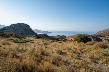 Çorak arazi, arkasında dağlar ve koylar olan sahil, açık mavi gökyüzü, sabahın erken saatleri, manzara, geniş açılı mercek.