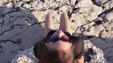 Genç bir kadın kayalık bir kıyı şeridinde oturuyor ve uzaklığa bakıyor. Kamera, kamera ondan uçsuz bucaksız ufka kaymadan önce objektife bakmak için döndüğünde onu yukarıda yakalar..