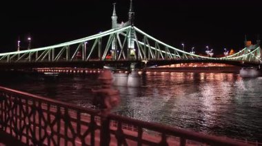 Budapeşte 'nin Özgürlük Köprüsü' nün büyüleyici gece manzarası. Karanlık gökyüzüne karşı parlayan ışıklar. Kamera ilerler, köprüyü, akan Tuna 'yı ve şehir trafiğini hafif açılı bir perspektiften yakalar..