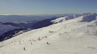 Slovakya 'daki Chopok Kayak Merkezi' nin zirvesinden çarpıcı bir panoramik manzara. Kamera karla kaplı dağları, parlak mavi gökyüzünü, kayak pistlerini ve mükemmel kış gününün tadını çıkaran kayakçıları yakalar..
