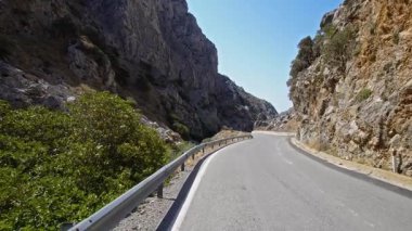 Girit 'teki Kotsifou Boğazı' nın dolambaçlı yolunda nefes kesici bir yolculuk. Kamera yavaş yavaş yokuş aşağı hareket ediyor, yüksek kaya oluşumlarıyla çevrili boş, eğimli asfalt yolu yakalıyor..