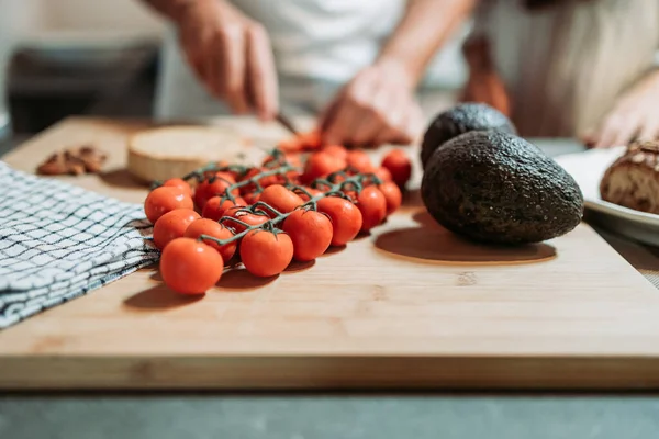 キッチンボード上のチェリートマトとアボカドのクローズアップ 食事の準備 背景の切断でぼやけた手 健康的な食事 — ストック写真
