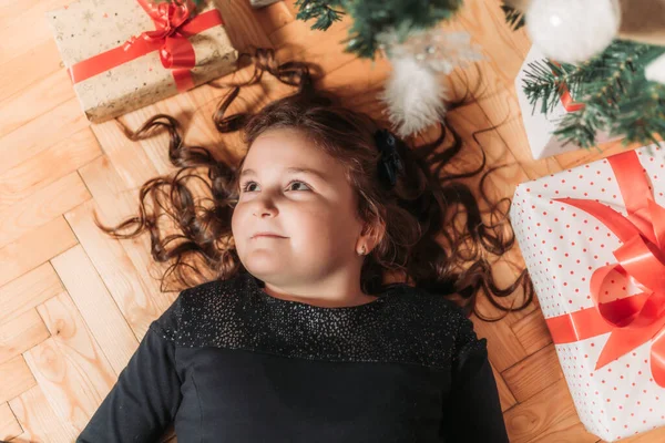 stock image Top view of a little brunette girl lying under the Christmas tree surrounded with gift boxes